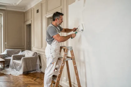 Peintre professionnel appliquant de la peinture blanche sur un mur intérieur avec un rouleau, dans un appartement parisien rénové